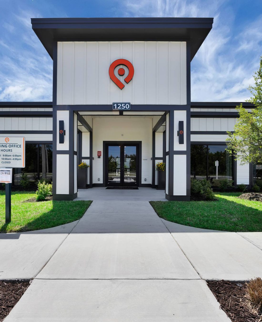 Modern leasing office building with glass doors, a sign, and accessible parking, surrounded by green lawn.