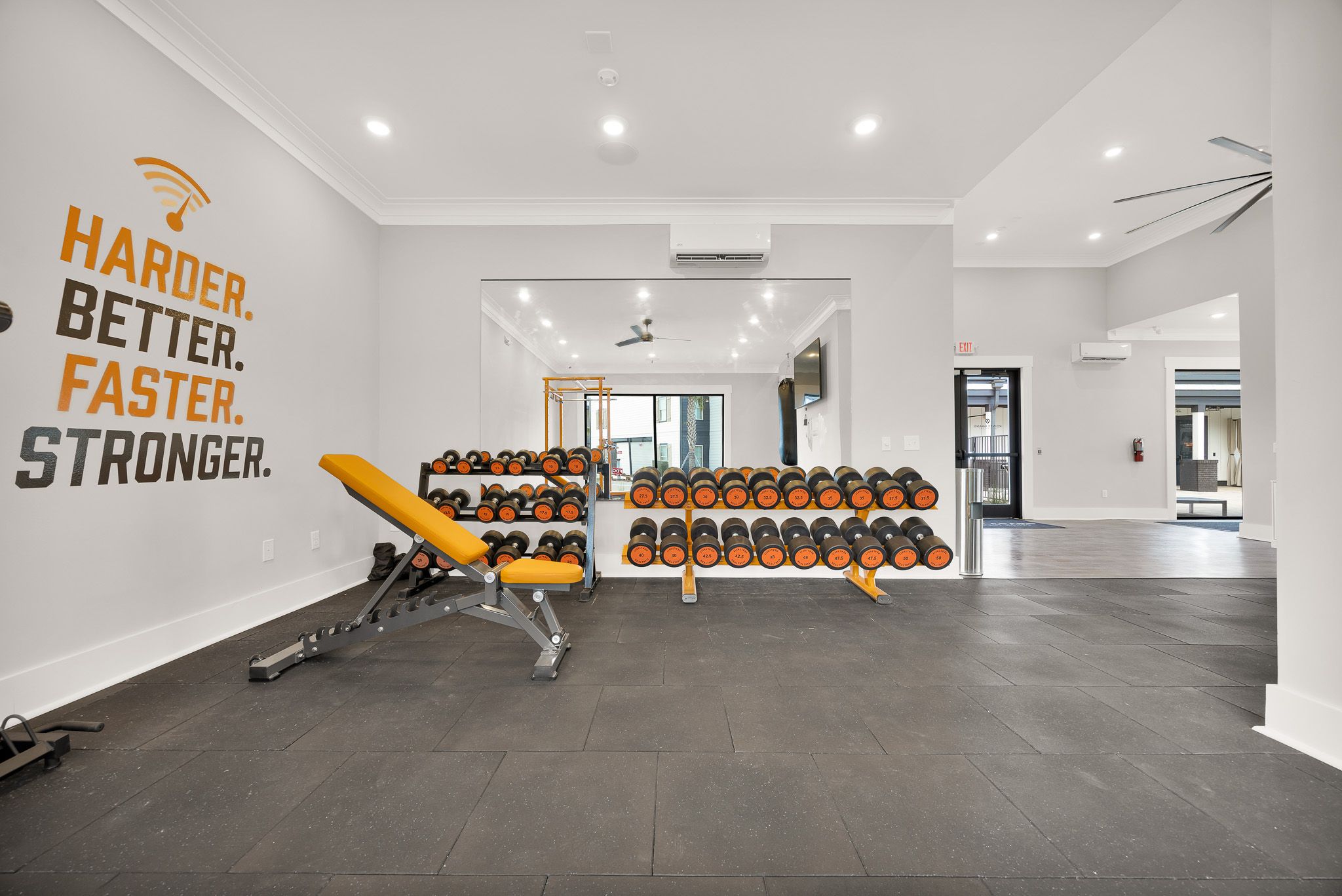 Modern gym with yellow workout bench, rows of dumbbells, and motivational quote on the wall.