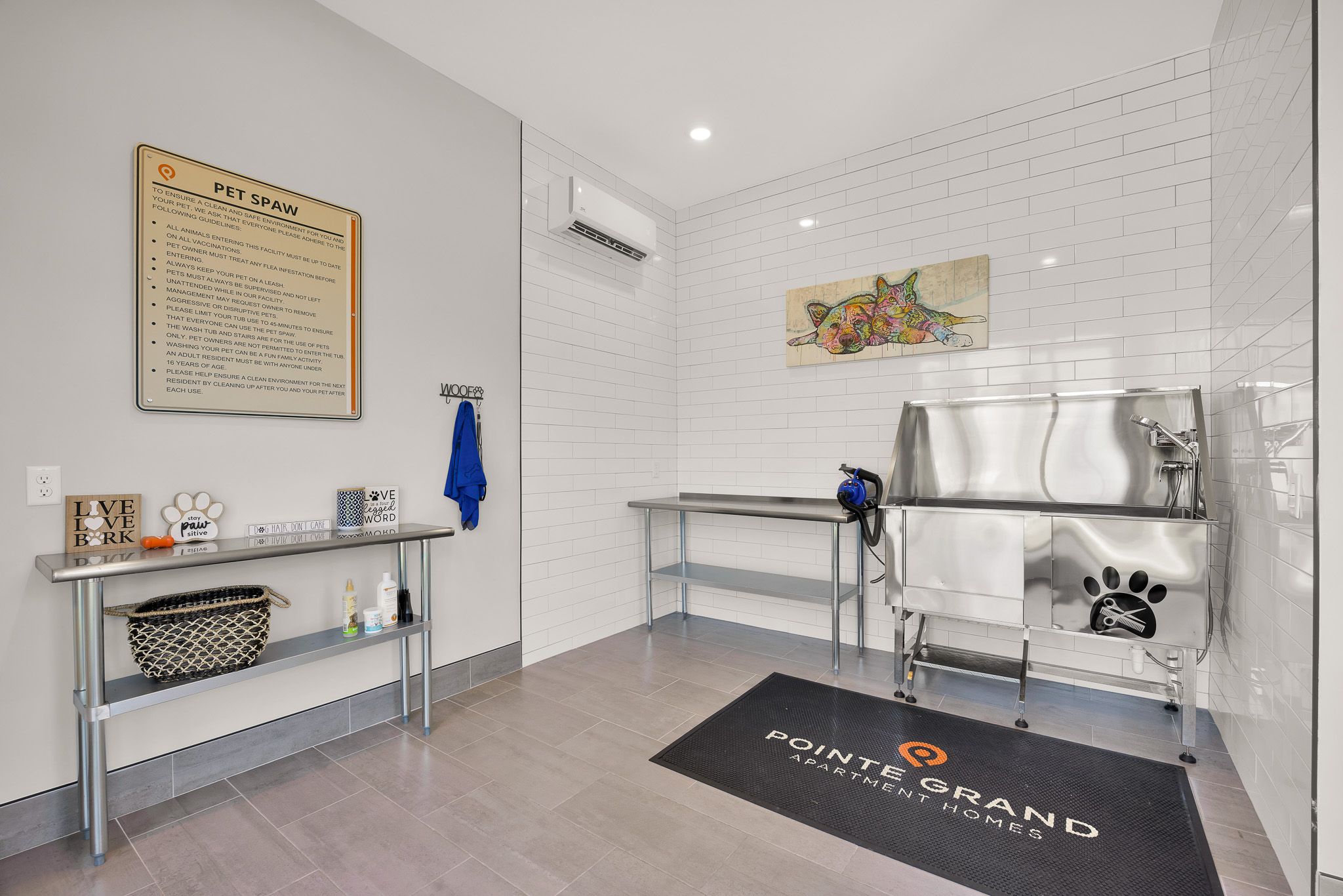 Modern pet wash station with metal tub, grooming tables, wall art, and pet care supplies.