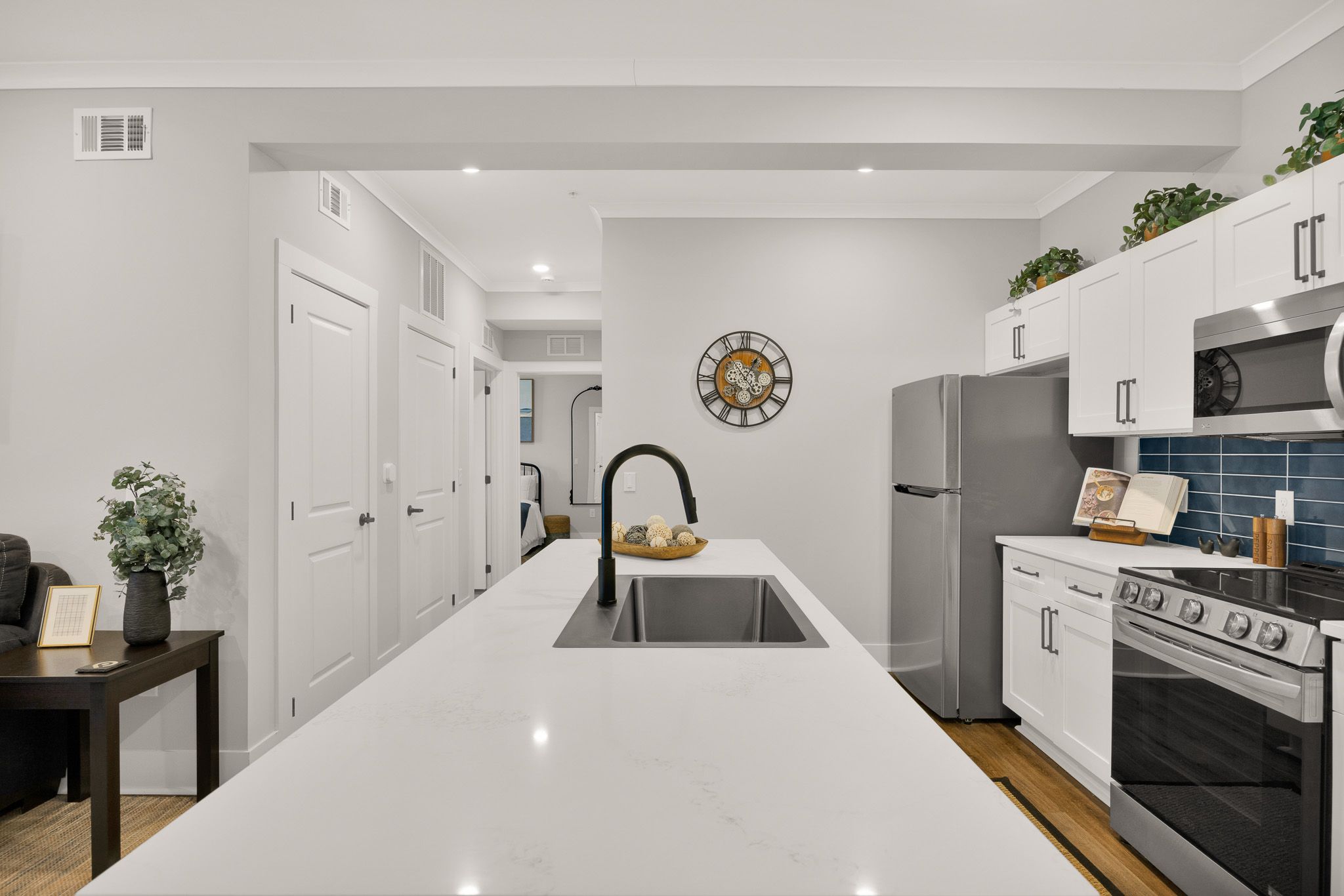 Modern kitchen with white cabinets, a large island sink, stainless steel appliances, and a wall clock.