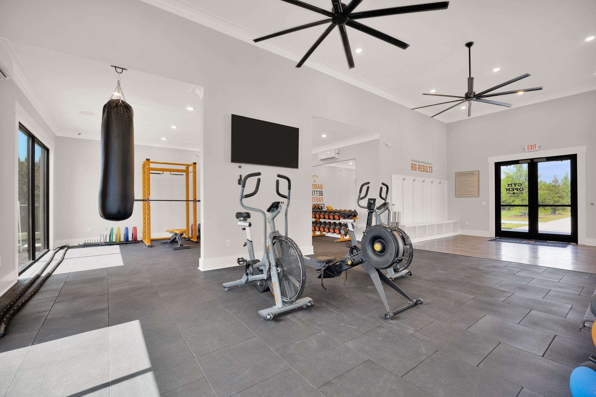 Modern gym with stationary bikes, punching bag, weights, fitness equipment, and large ceiling fans.