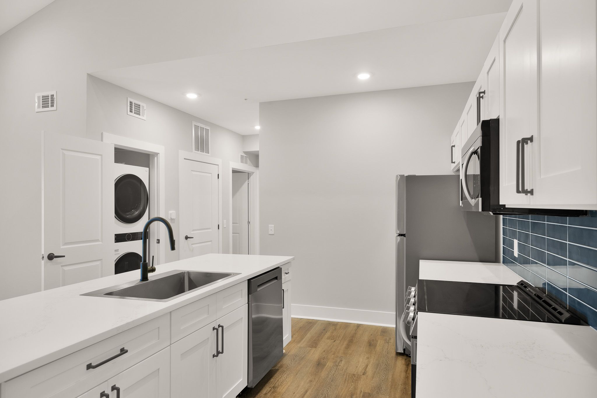 Modern kitchen with white cabinets, a blue tile backsplash, and a stacked washer and dryer in the corner.