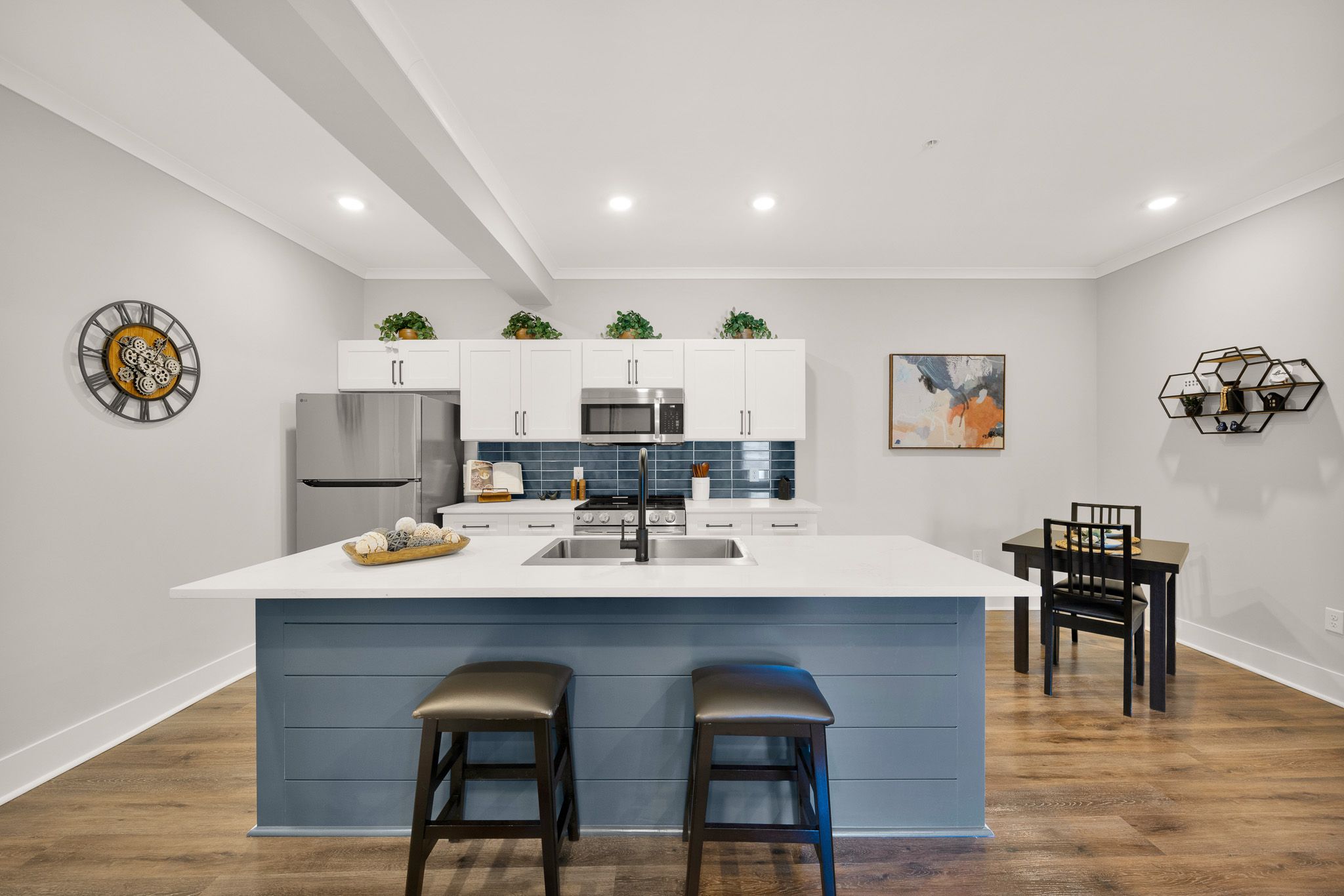 Modern kitchen with white cabinets, blue island, and dining area, featuring wood floors and decorative accents.
