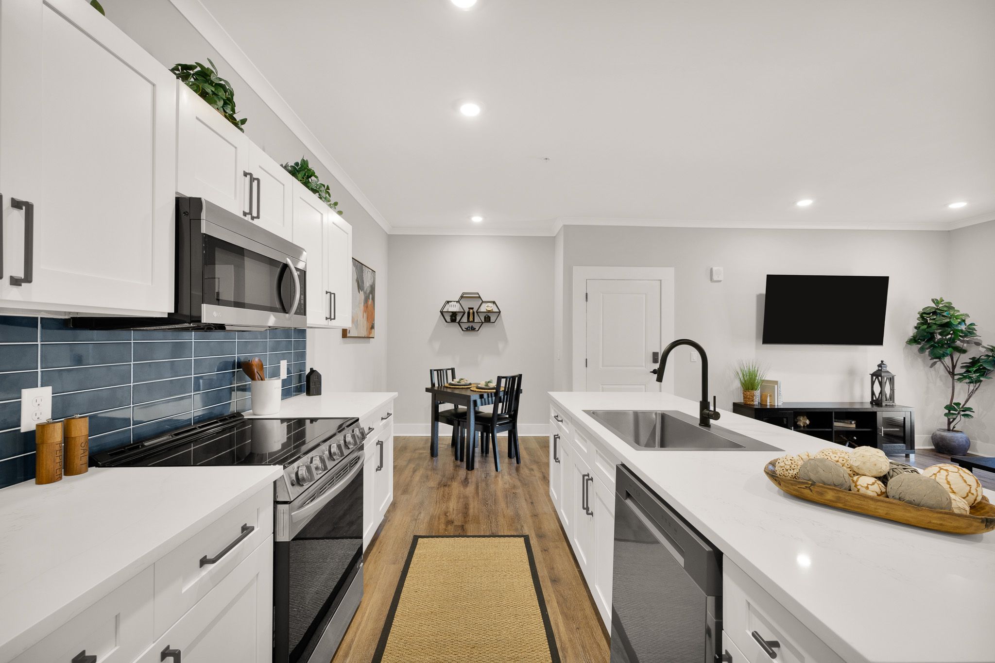 Modern kitchen with white cabinets, stainless steel appliances, and a dining area in the background.