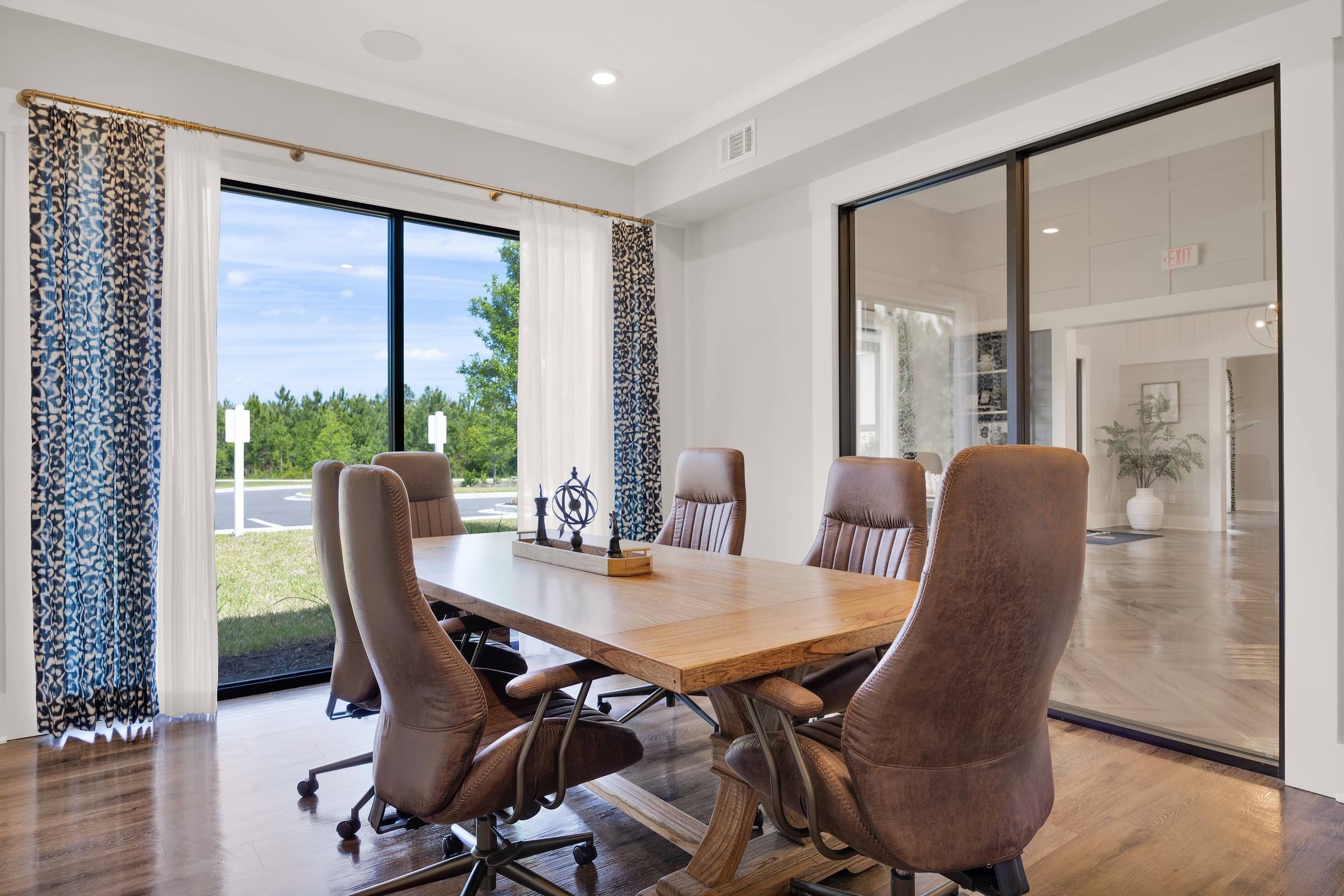 A modern conference room with a wooden table, leather chairs, large windows, and patterned curtains.
