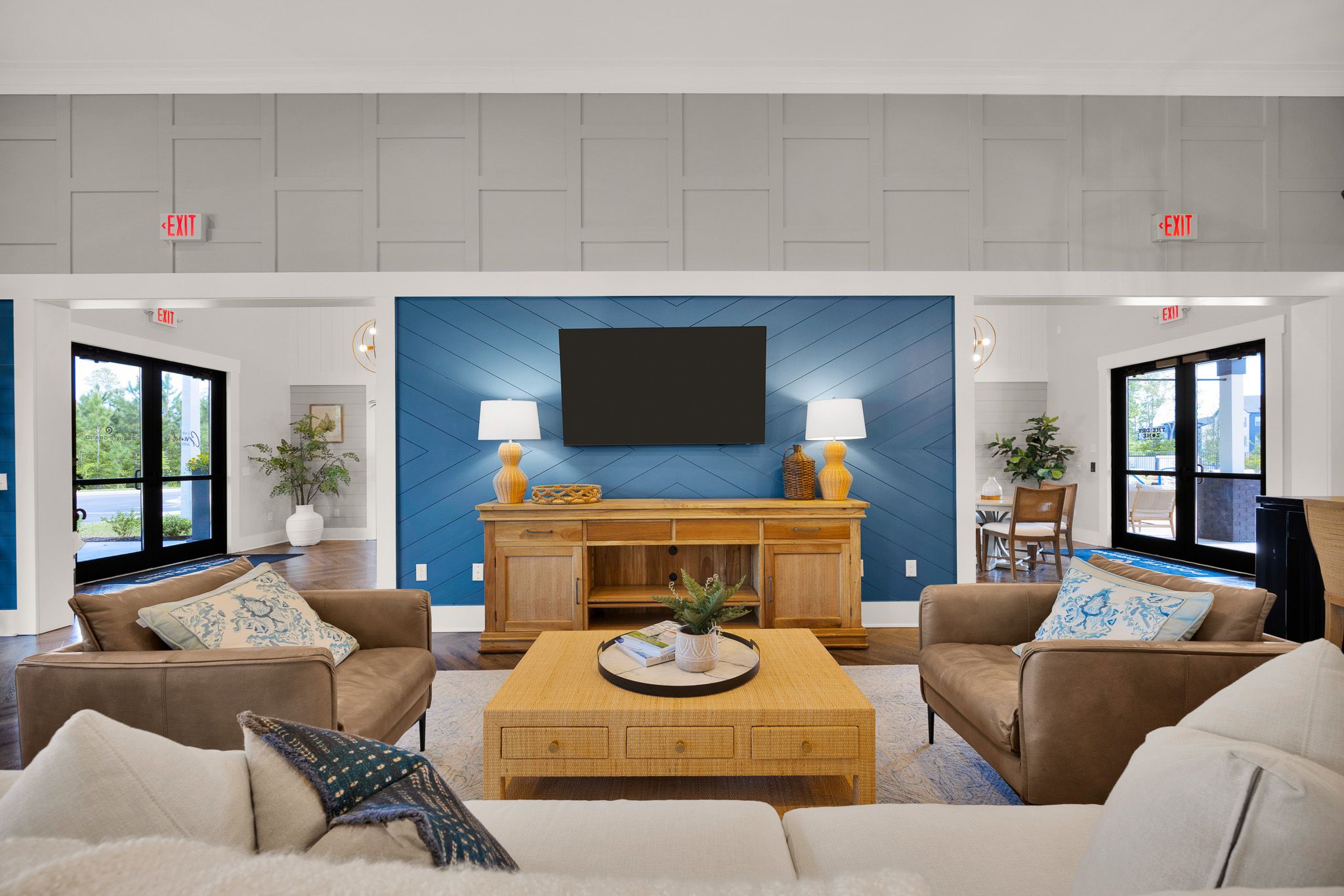 Modern living room with neutral sofas, a wooden coffee table, and a blue accent wall featuring a TV and lamps.
